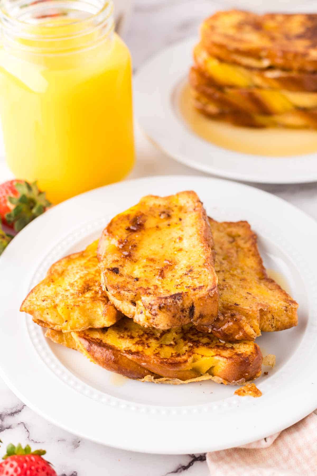 challah french toast with syrup on a round plate with juice to the side.