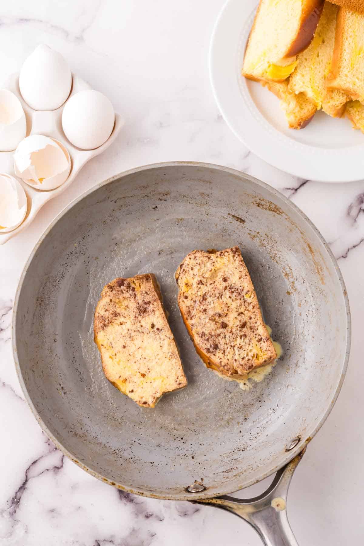 pan cooking two pieces of challah french toast.