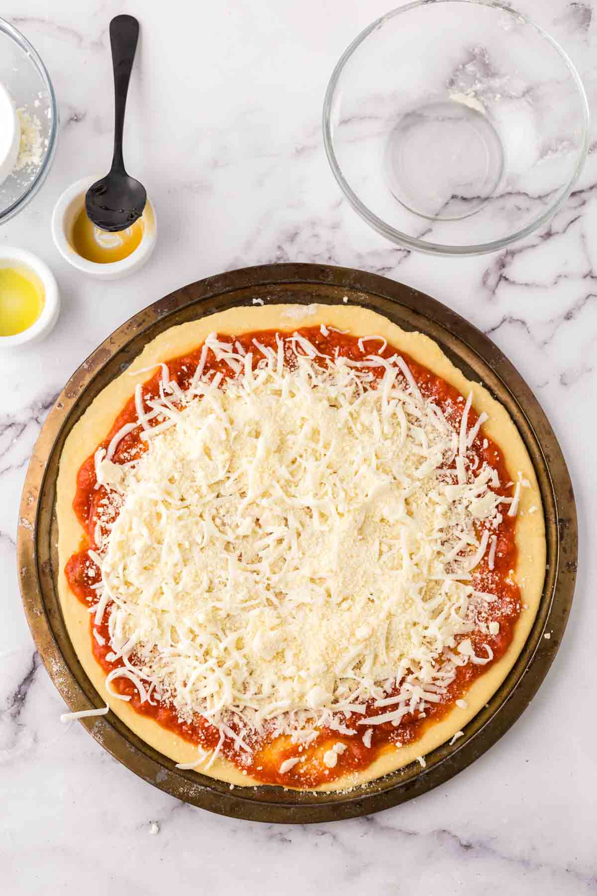 round pizza tray with raw dough on top with cheese and sauce.