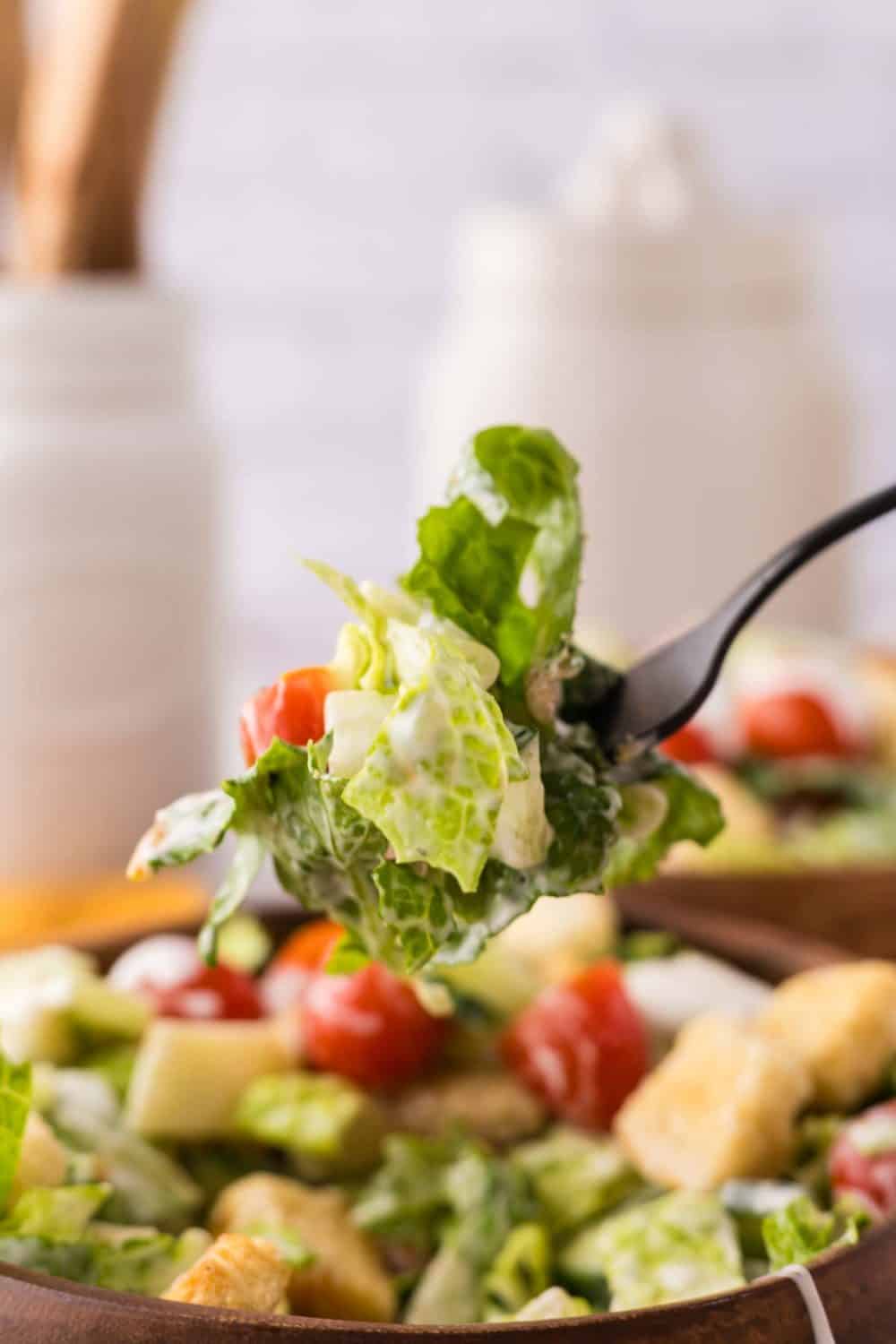 forkful of chefs salad over a wooden bowl.