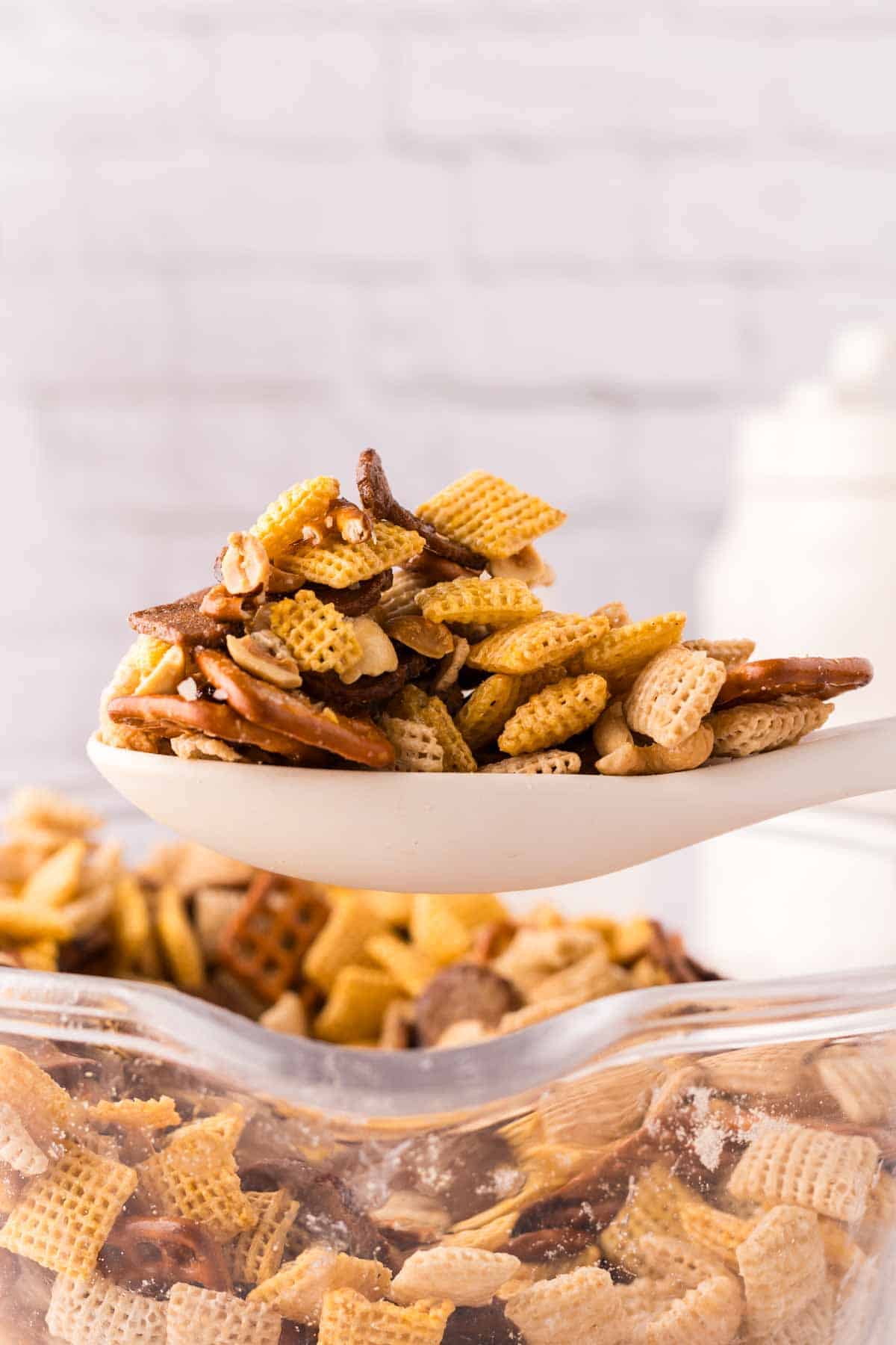 clear mixing bowl in the progress of making chex mix recipe with a wooden spoon.