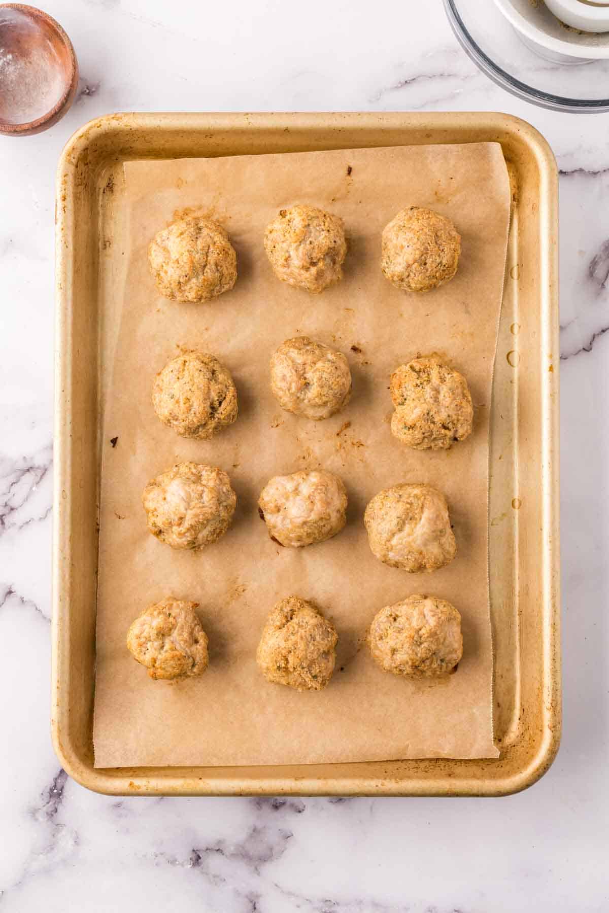 chicken meatballs lined on parchment on a baking tray.