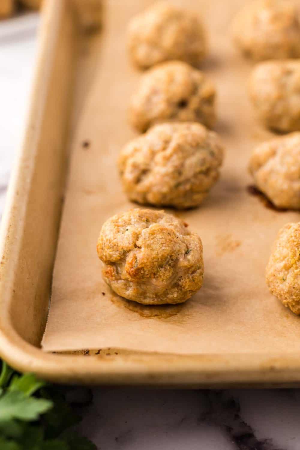 chicken meatballs lined on parchment over cookie trays.