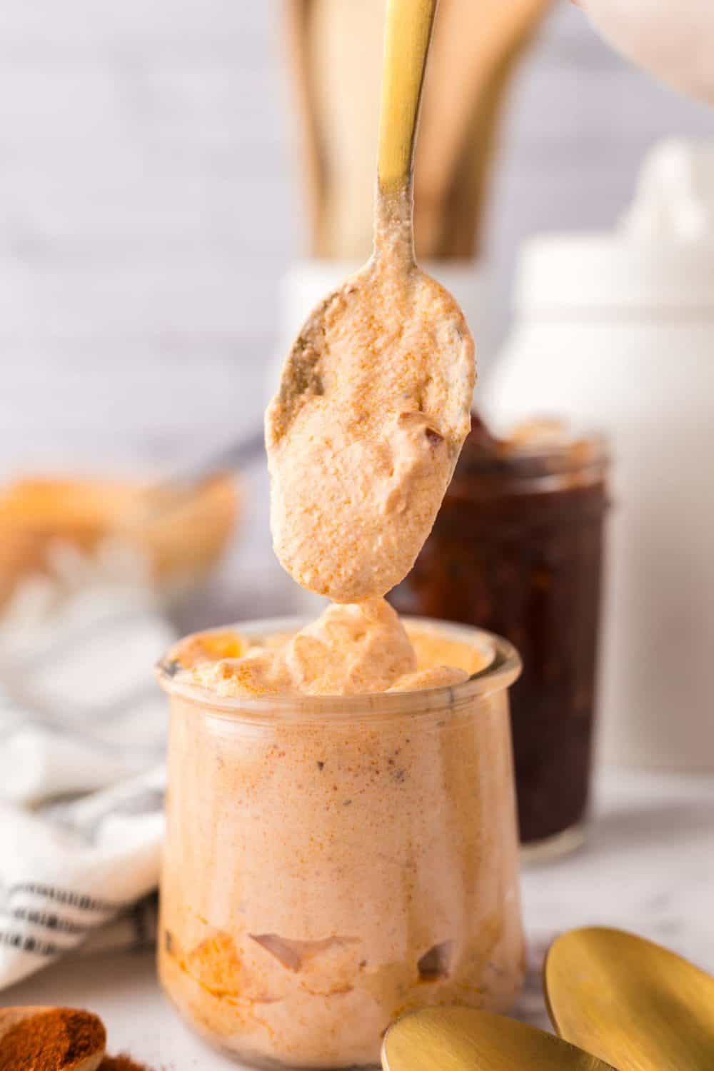 golden spoonful of chipotle sauce over a small glass jar of sauce.