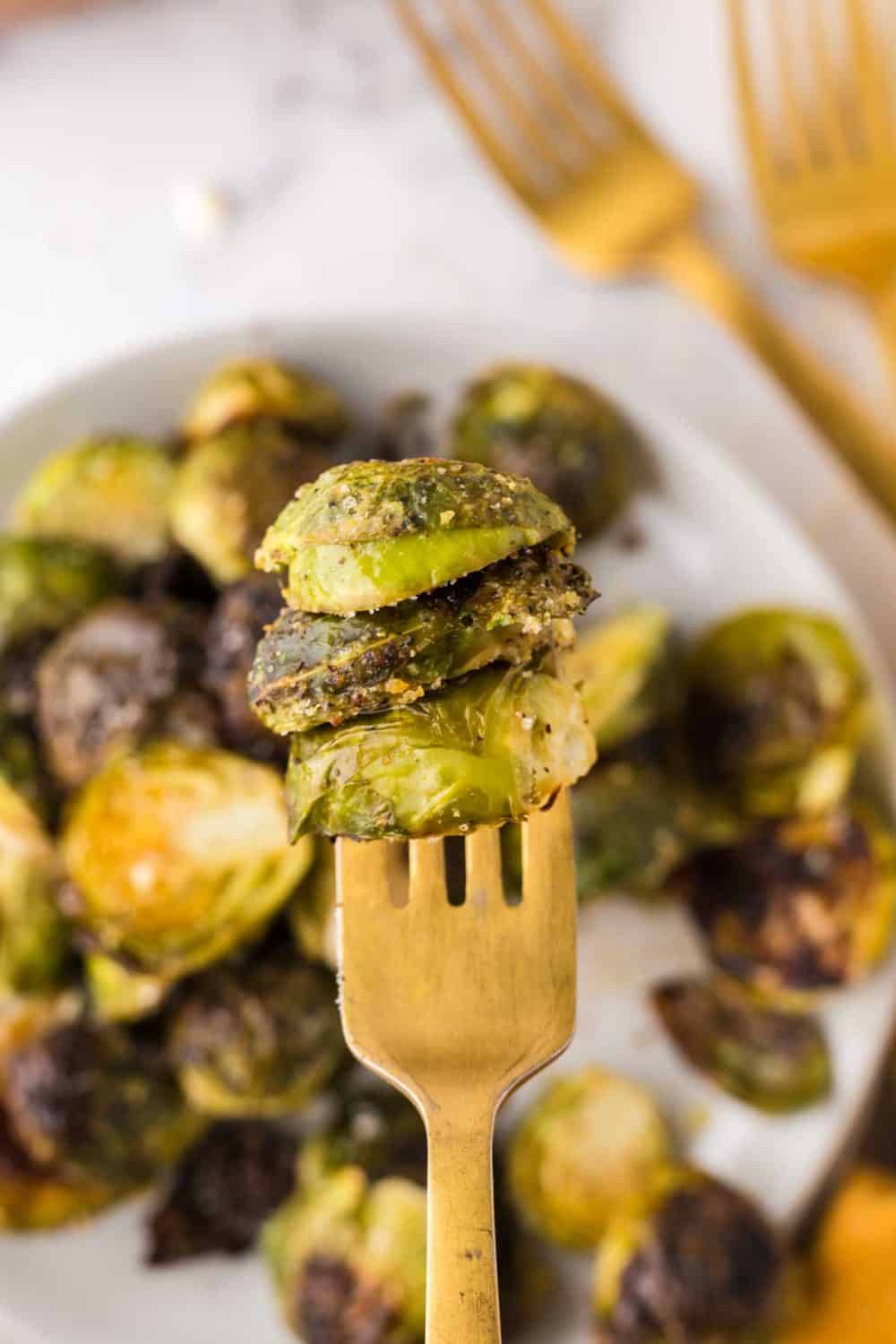 Oven Baked Brussels Sprouts on a golden fork over a white plate filled with them.