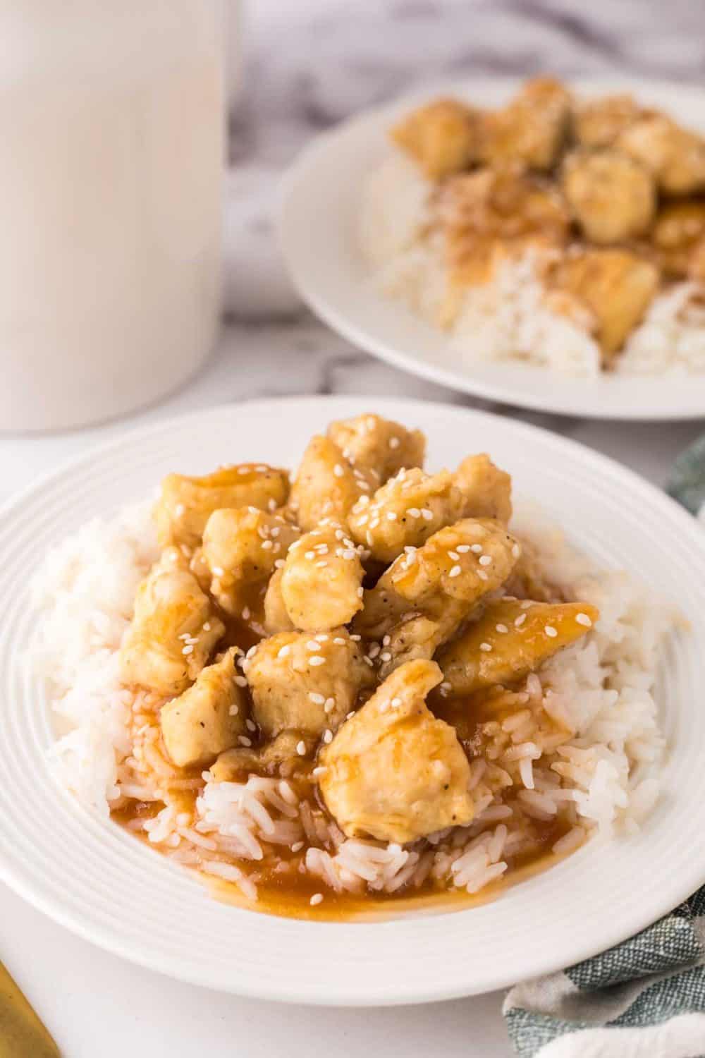 sweet and sour chicken over rice on a white plate.
