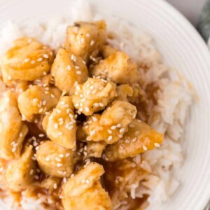 sweet and sour chicken over rice on a white plate.