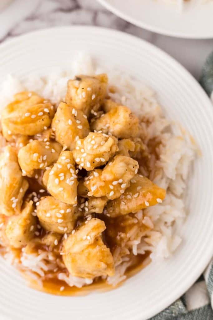 sweet and sour chicken over rice on a white plate.