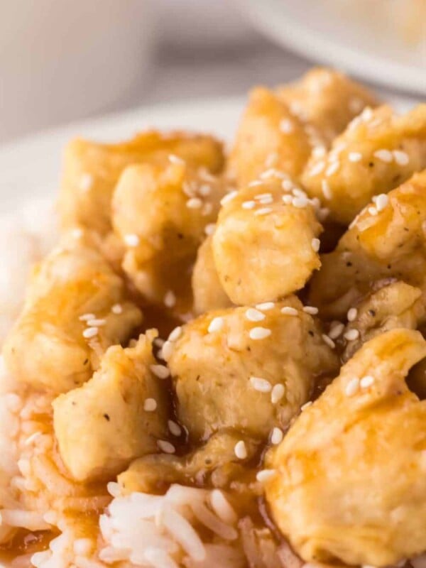 sweet and sour chicken over rice on a white plate.