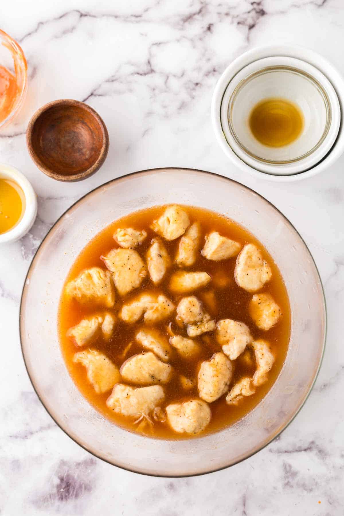 clear glass bowl with diced chicken and portioned ingredients for sweet and sour chicken.