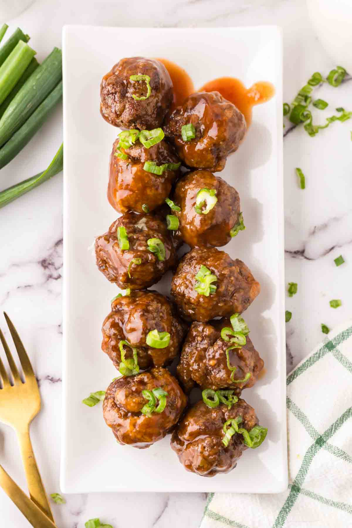 Two rows of sweet and sour sauce covered meatballs on a long rectangle plate.