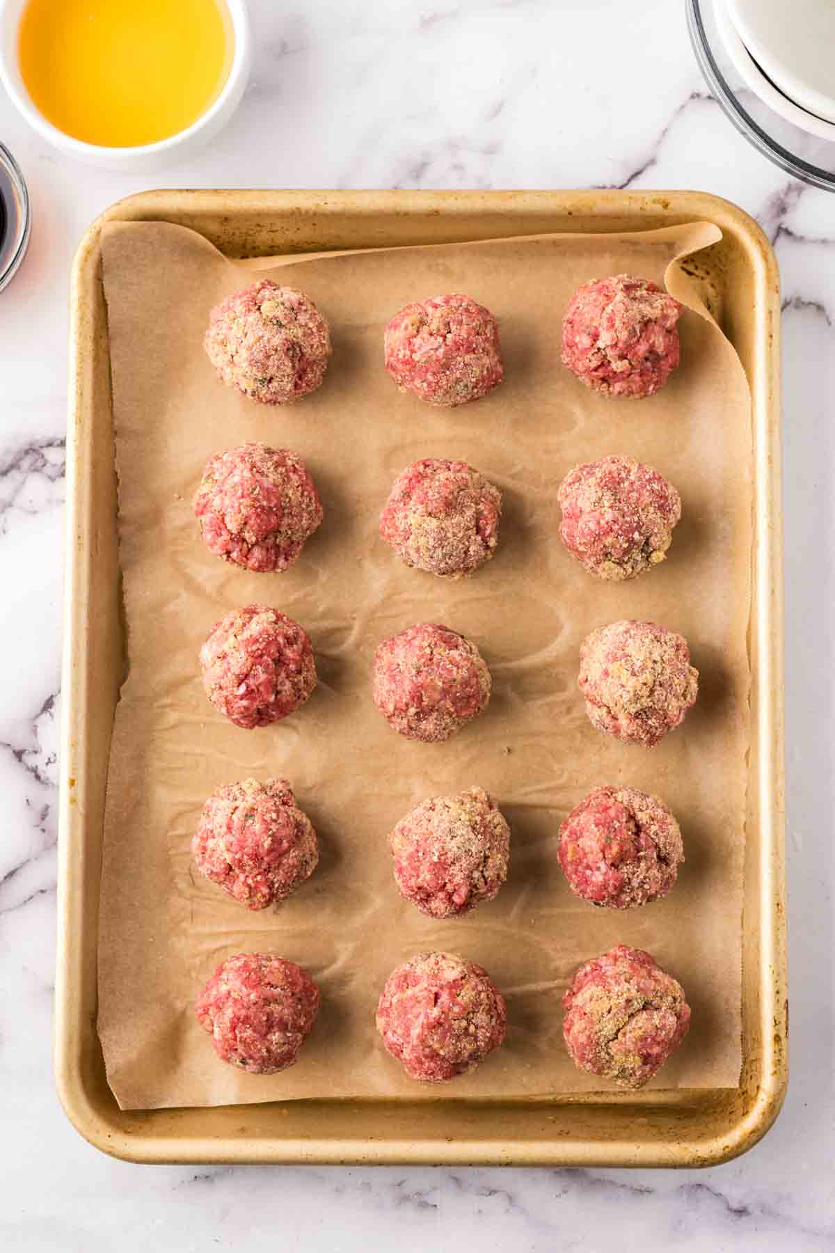Baking sheet with raw round meatballs over parchment.