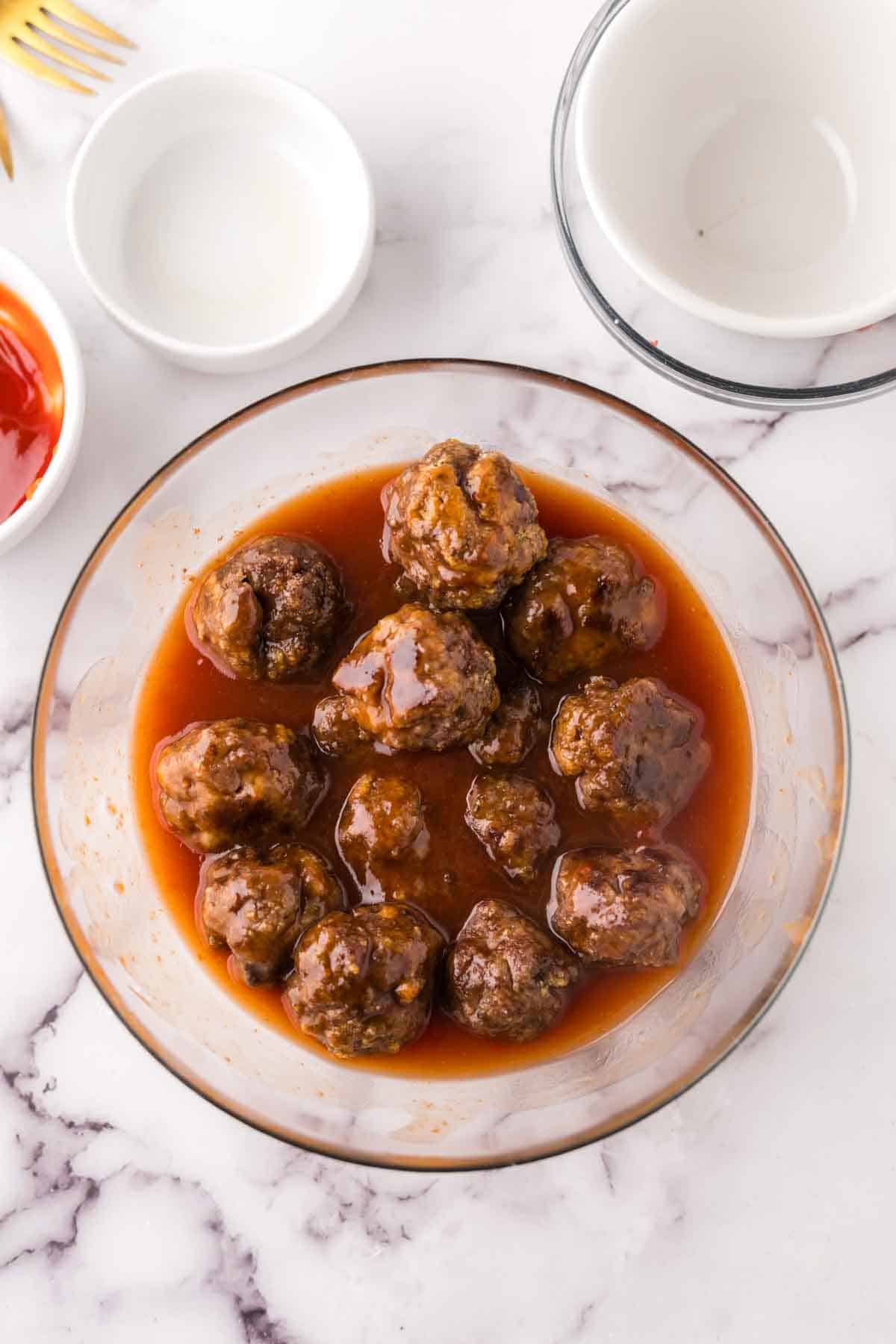 Meatballs in a clear white bowl covered in sweet and sour sauce.