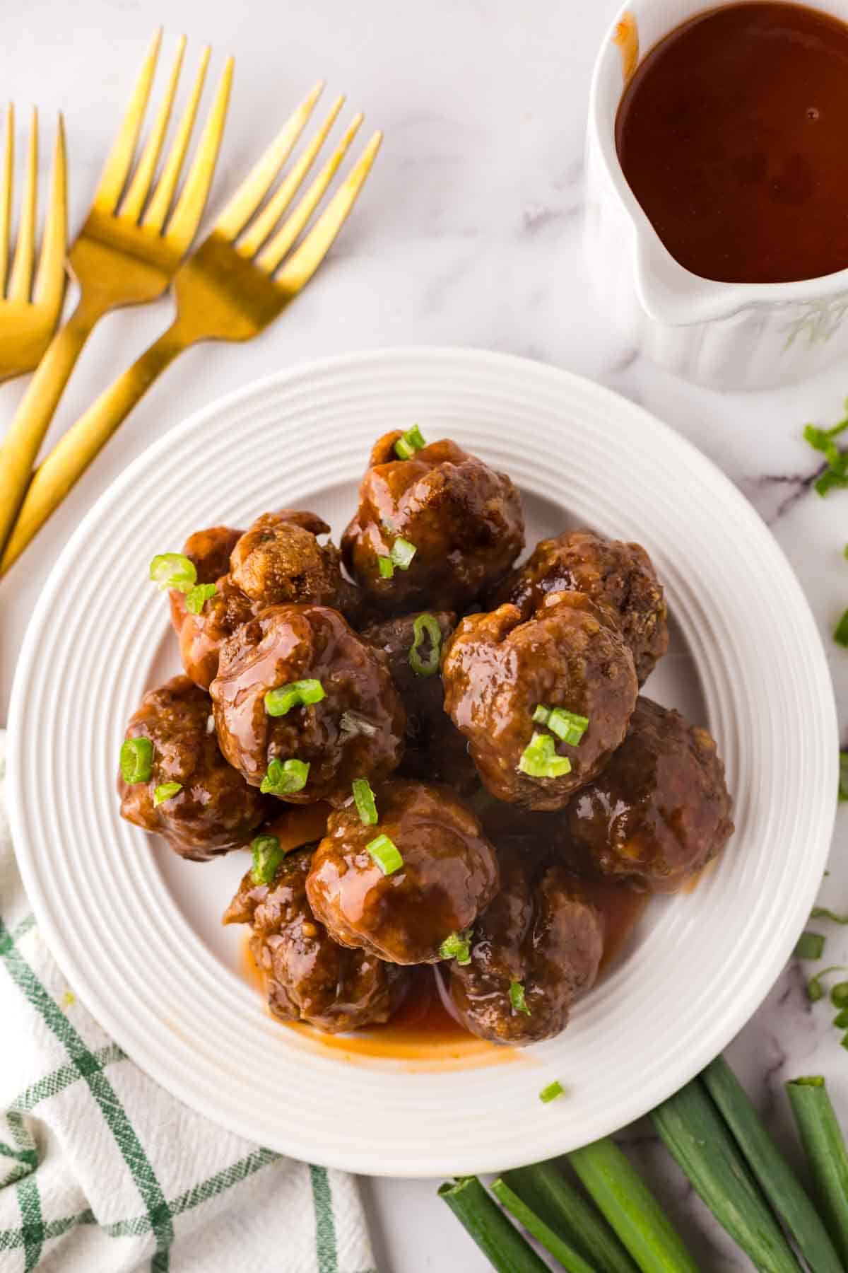 Stack of sweet and sour meatballs on a round white plate with golden forks to the side.