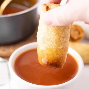 Dipping an egg roll into a bowl of sweet and sour sauce.