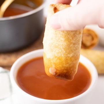 Dipping an egg roll into a bowl of sweet and sour sauce.