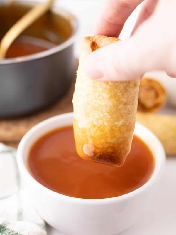 Dipping an egg roll into a bowl of sweet and sour sauce.