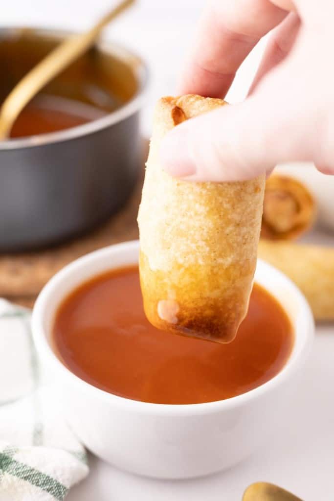 Dipping an egg roll into a bowl of sweet and sour sauce.