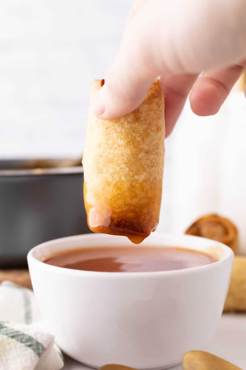 Eggroll getting dipped into a bowl of sweet and sour sauce. 