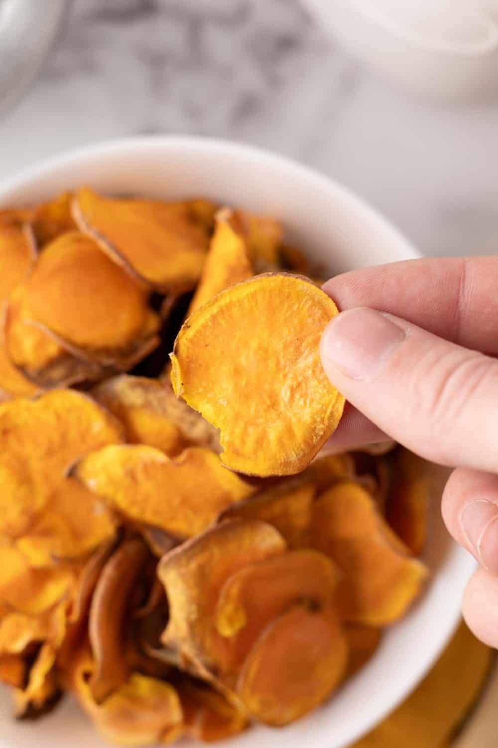 hand holding a sweet potato chip over a bowl full.