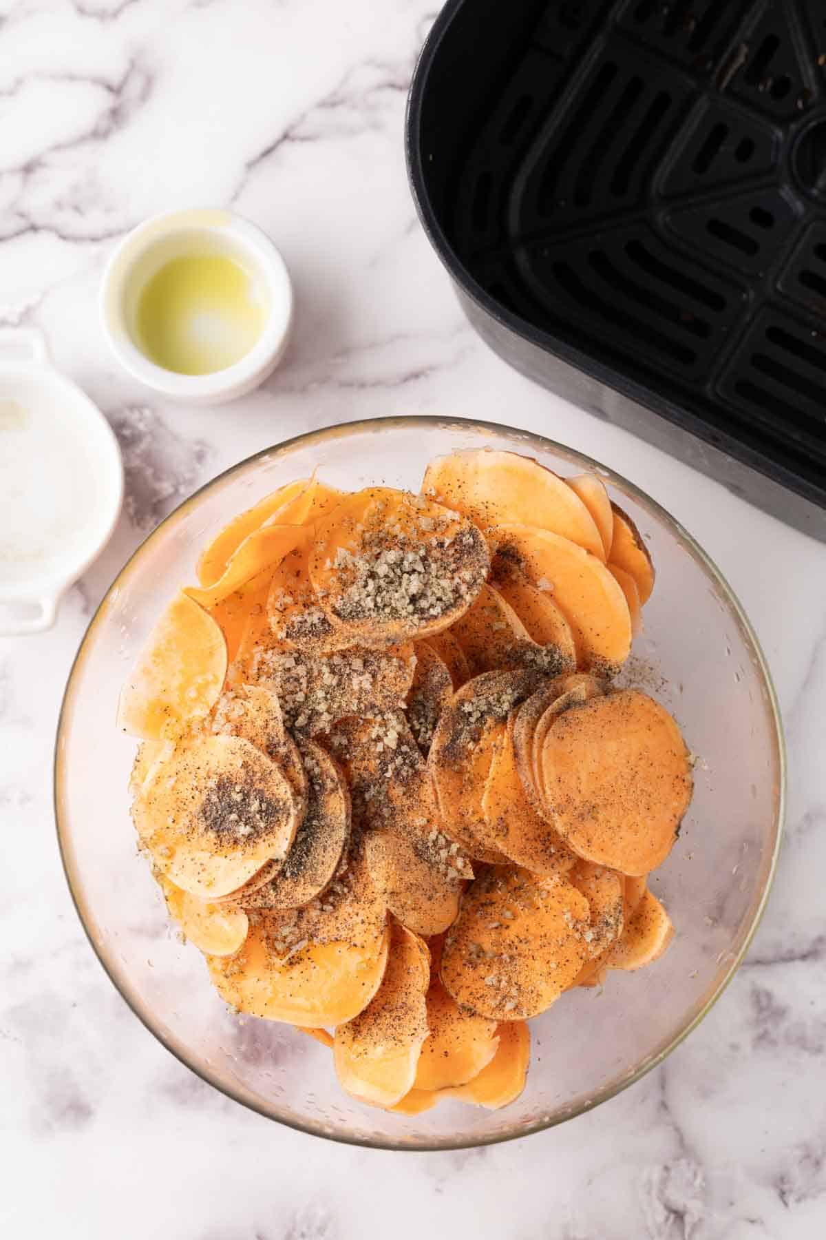 sweet potato chips in a bowl with seasoning before air frying.