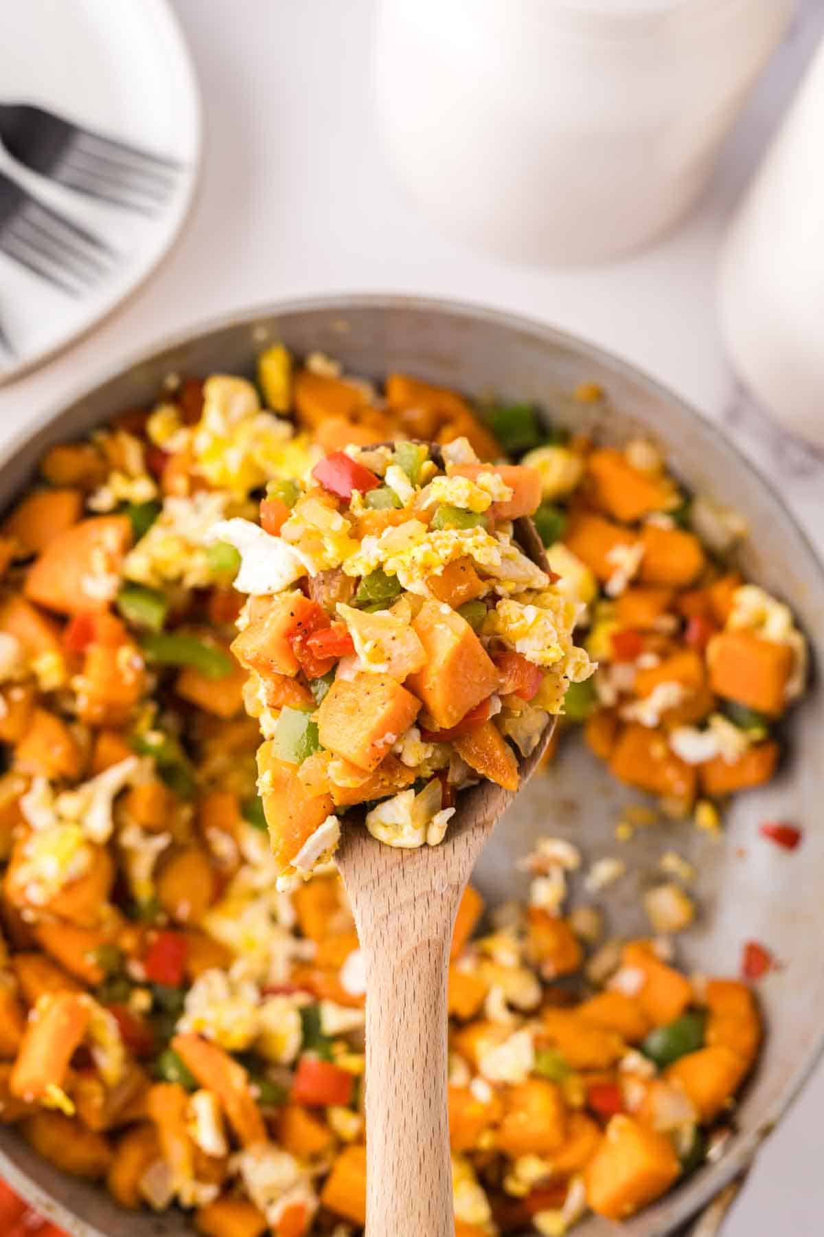 wooden spoon with sweet potato hash held over a pan of hash.