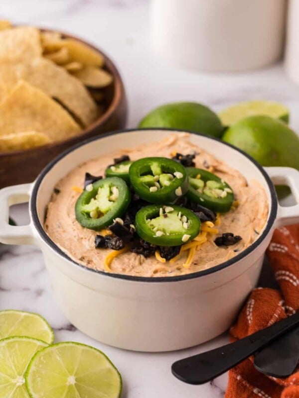 a white bowl of a taco dip topped with sliced fresh jalapeños and cheese.