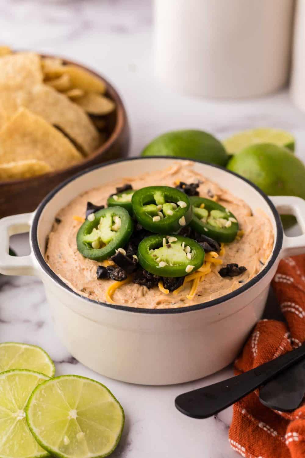 a white bowl of a taco dip topped with sliced fresh jalapeños and cheese.