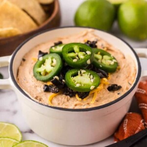 a white bowl of a taco dip topped with sliced fresh jalapeños and cheese.