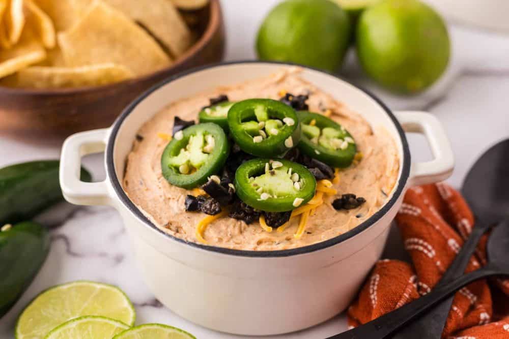 a white bowl of a taco dip topped with sliced fresh jalapeños and cheese.