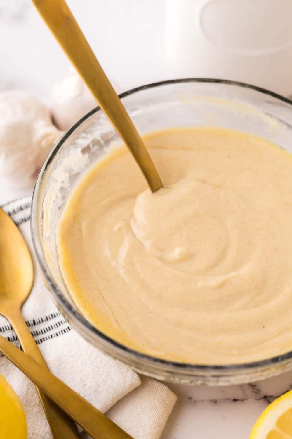 tahini dressing in clear glass mixing bowl with a golden spoon in it.