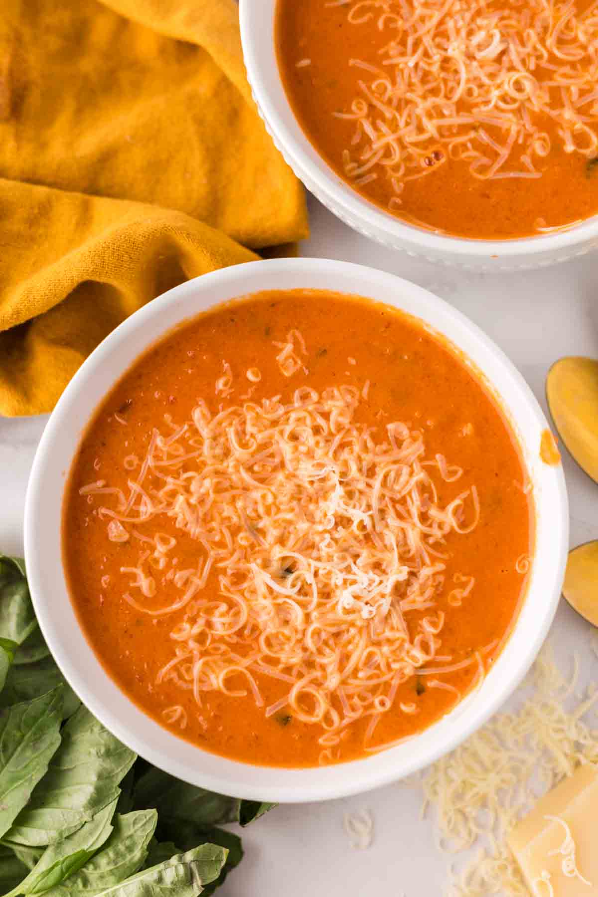 two white bowls with tomato basil soup and cheese on top.