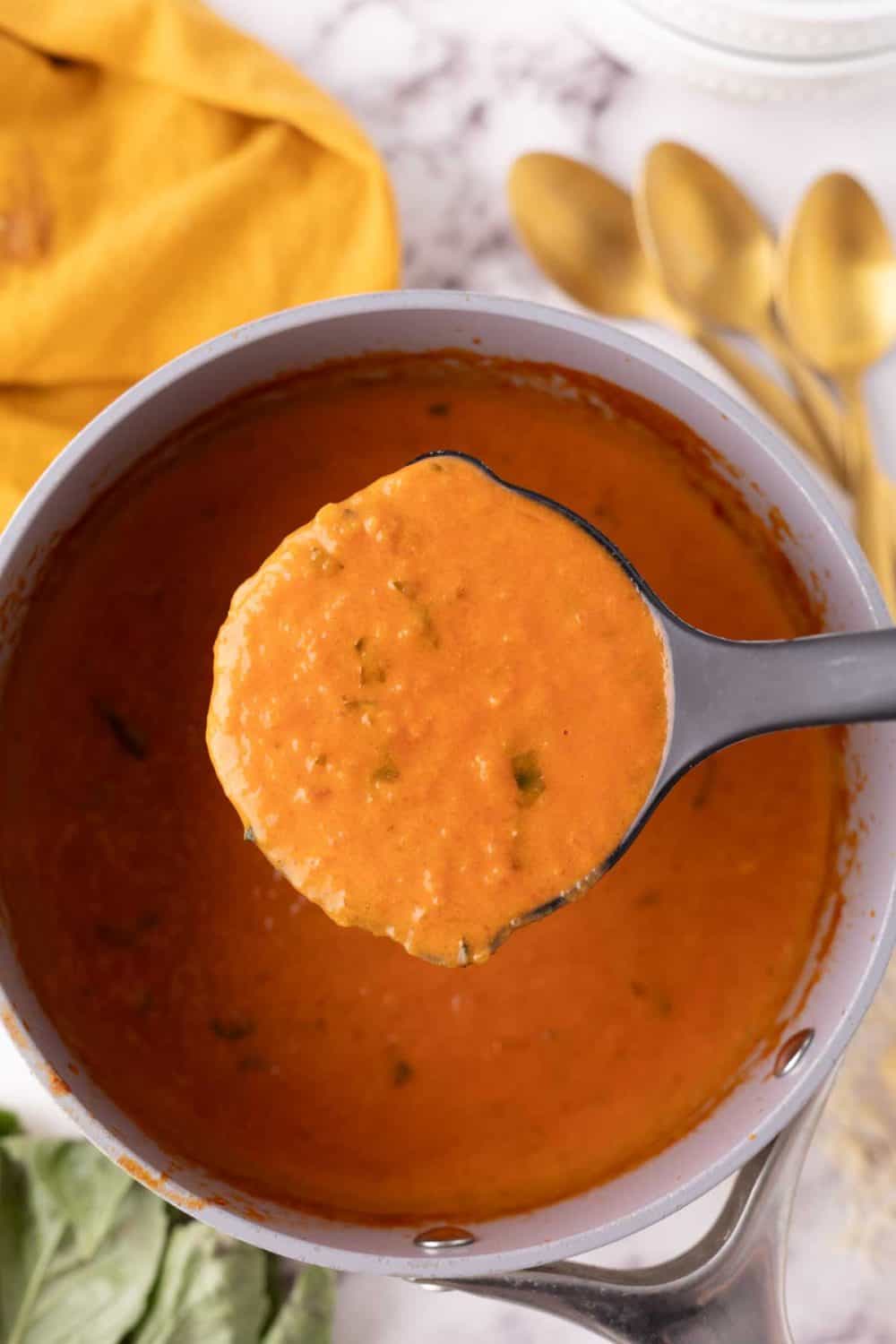 ladle of tomato basil soup over the pot cooking.