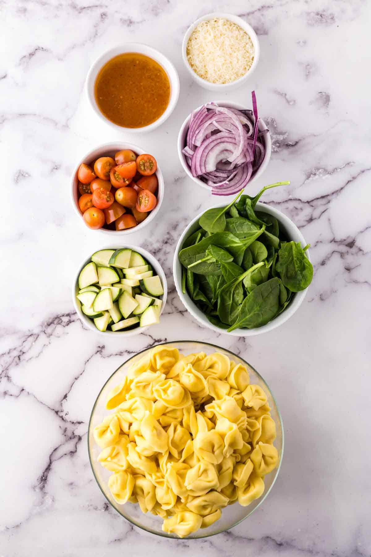 portion bowls each raw ingredient to make tortellini salad.