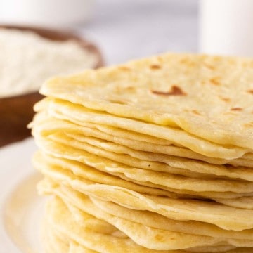 homemade tortillas in a tall stack on a round white plate.