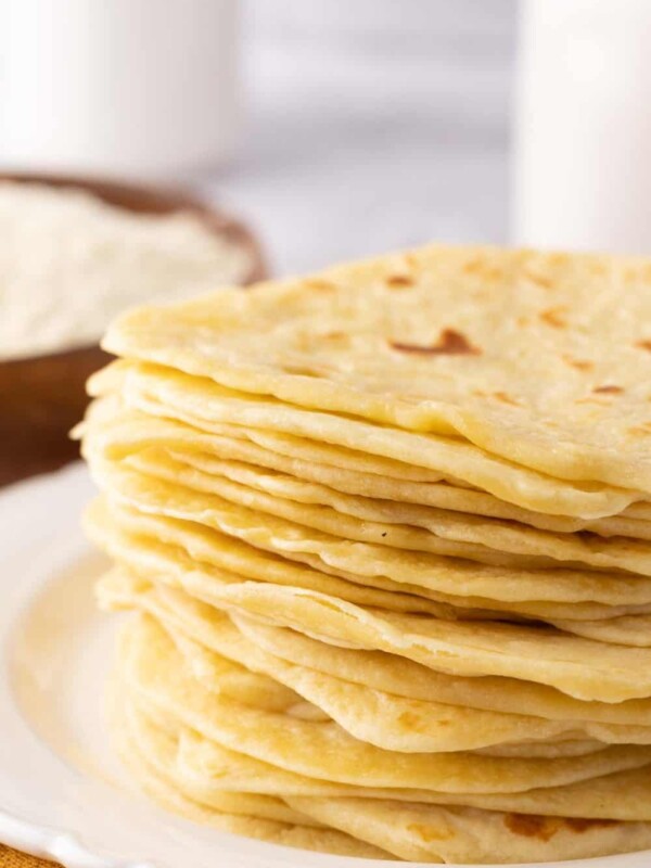 homemade tortillas in a tall stack on a round white plate.