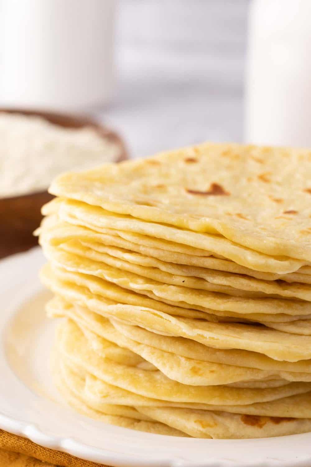homemade tortillas in a tall stack on a round white plate.
