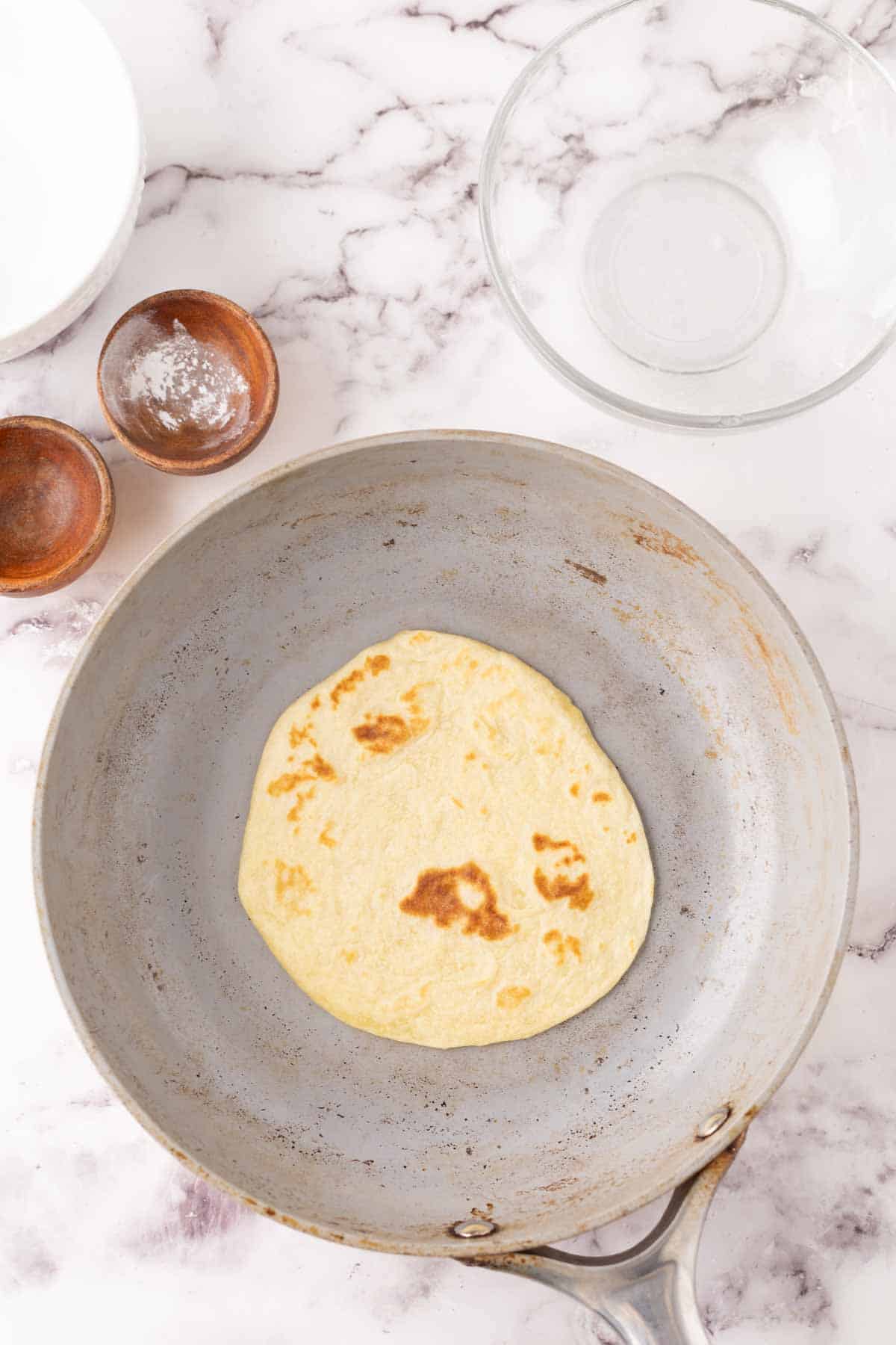 one homemade tortilla on a pan in the process of browning.