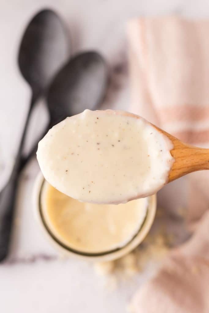 wooden spoon over a small glass jar with white pizza sauce.