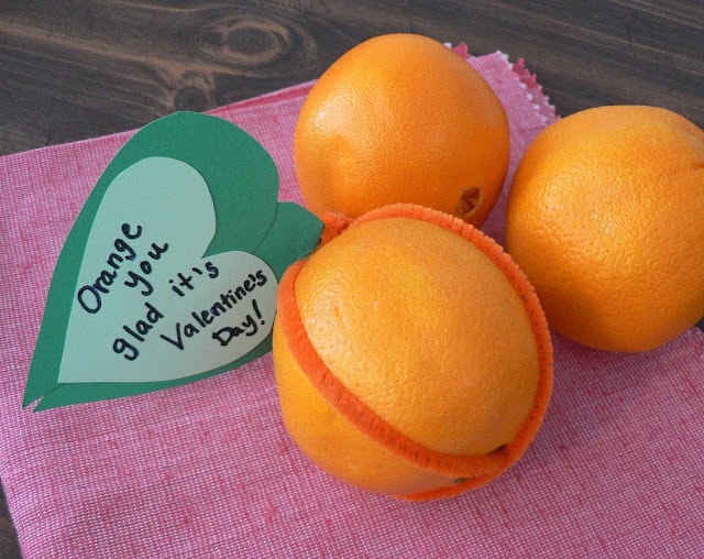 An orange with a heart-shaped green leaf that says, Orange you glad it's Valentine's Day.