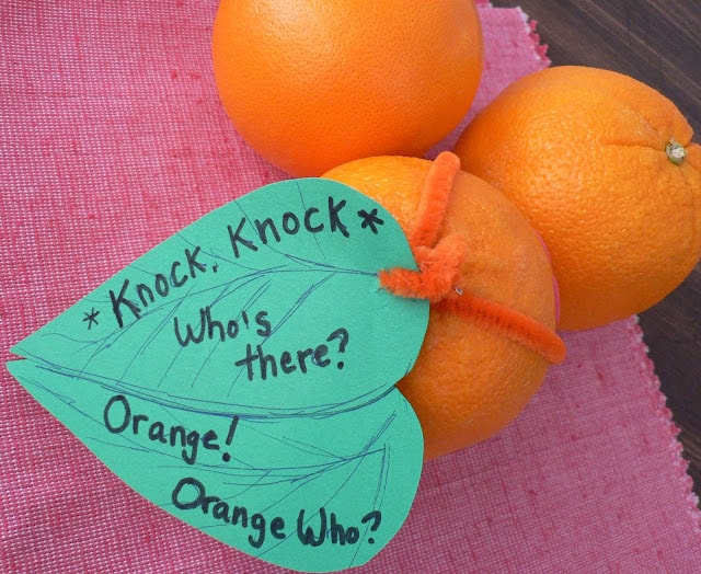 An orange with a heart-shaped green leaf that says, Knock Knock Who's there Orange Orange who.