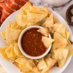 round white plate with homemade baked corn tortilla chips with a bowl of salsa in the middle.