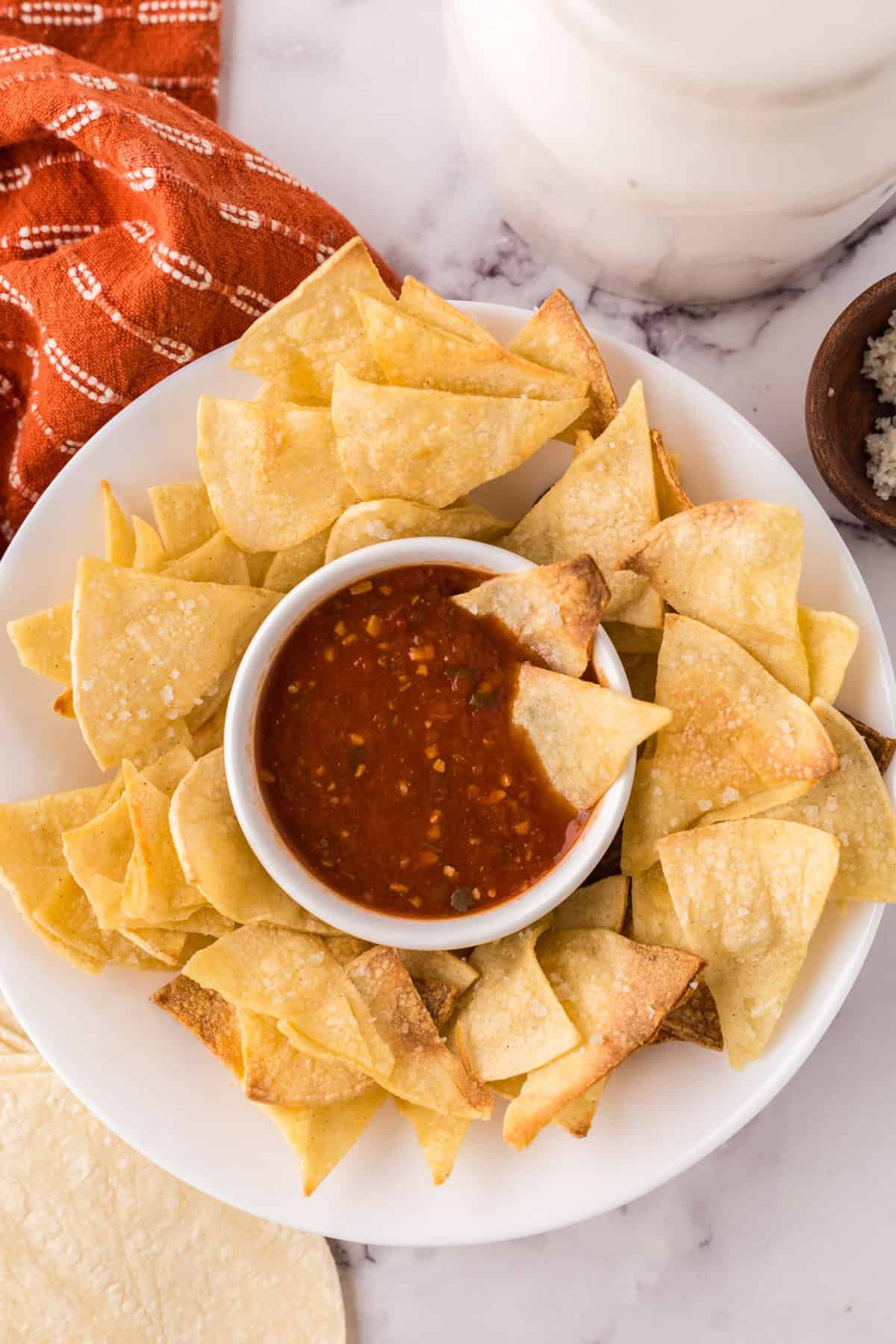 round white plate with homemade baked corn tortilla chips with a bowl of salsa in the middle.