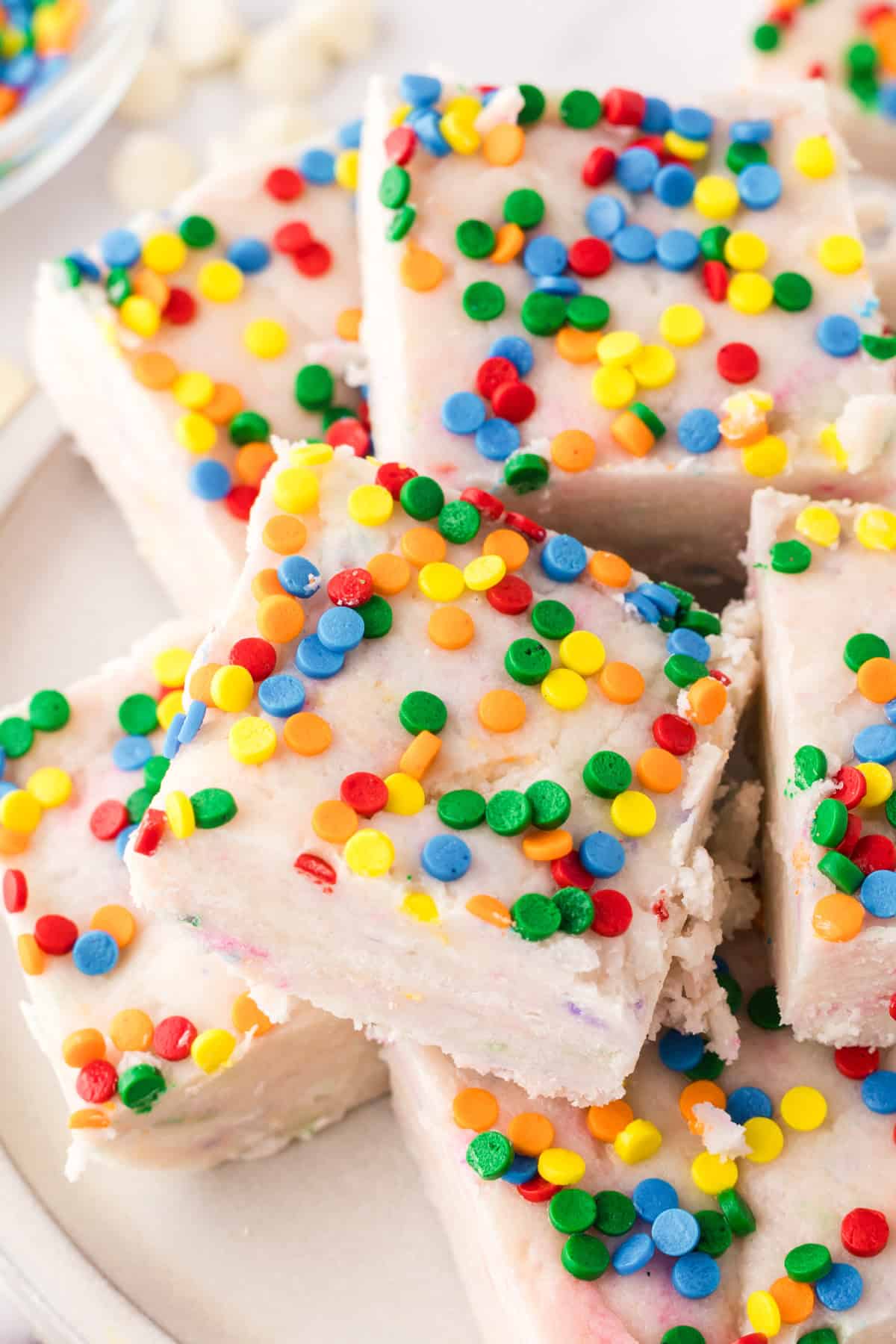 a plate of rainbow sprinkled square pieces of cake batter fudge.