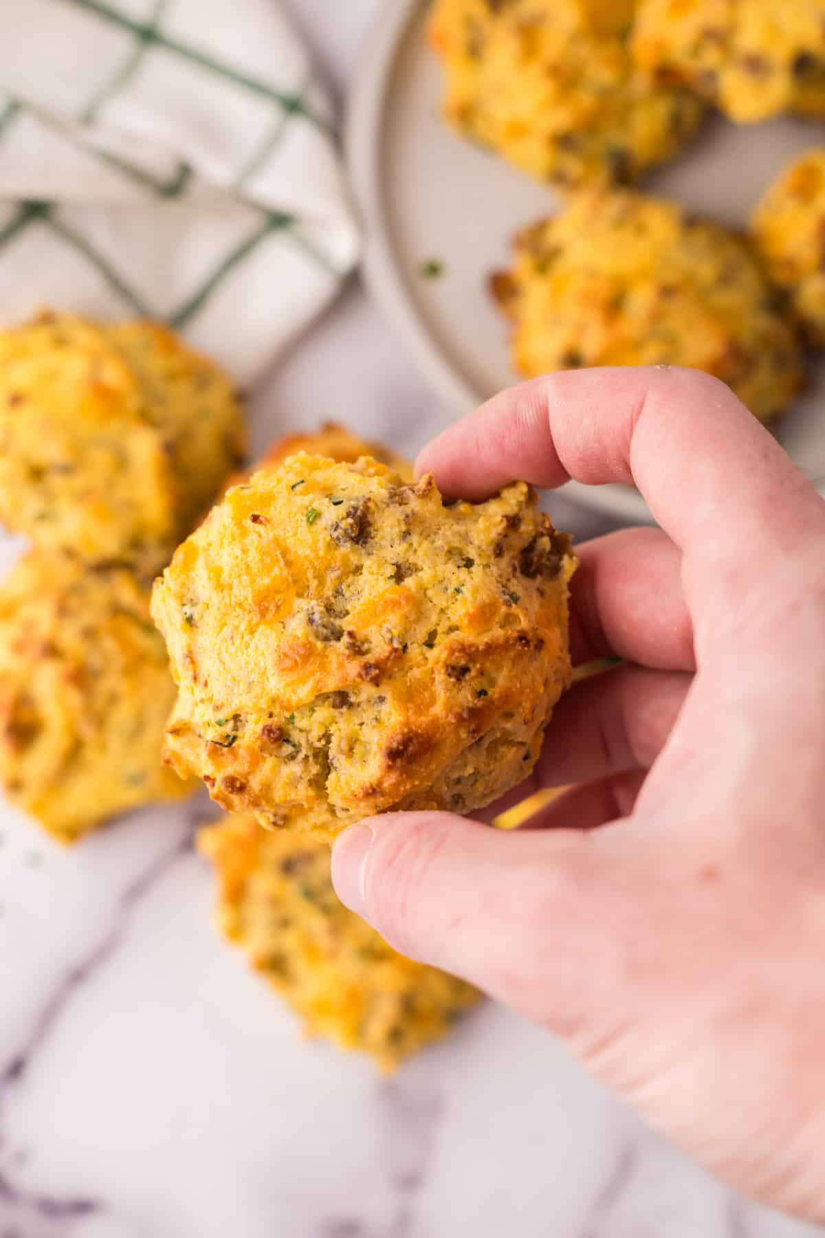 POV hand holding one round golden brown cheddar sausage biscuits ready to eat.