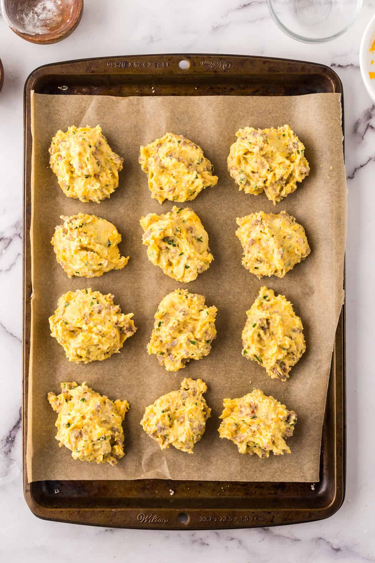 sheet pan with parchment with balls of cheddar biscuit dough ready to bake.