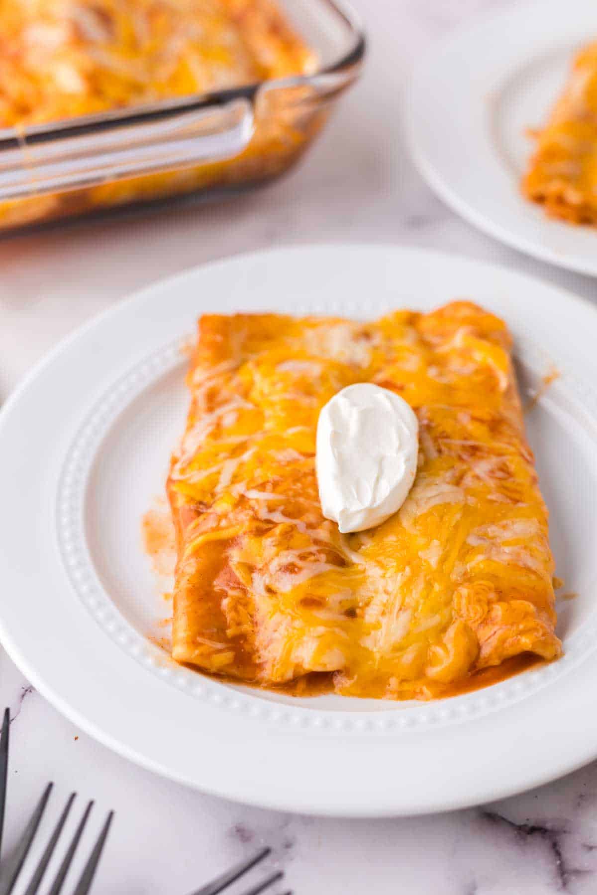 cheese enchiladas on a white plate with sour cream on top.