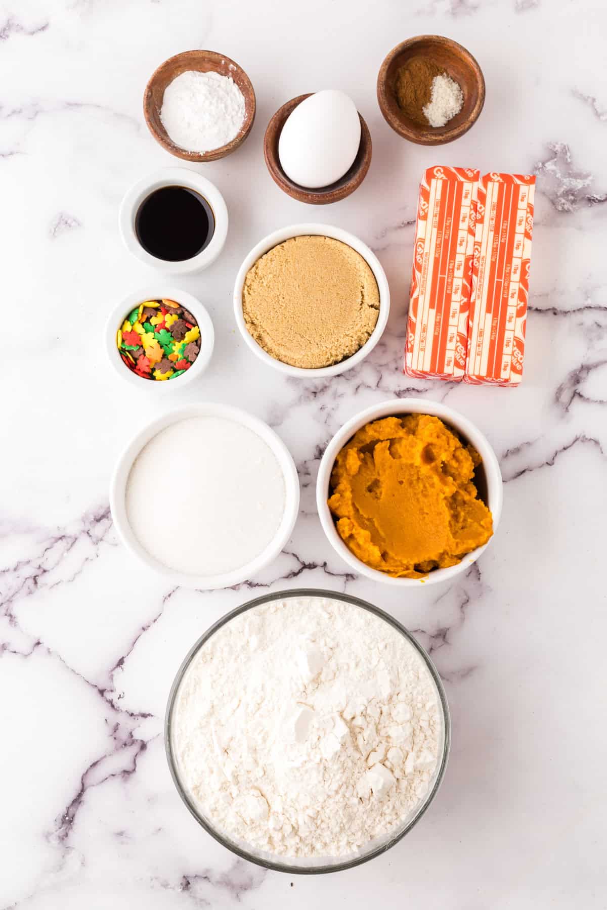 portion bowls each with raw ingredients to make pumpkin cookies with sprinkles.