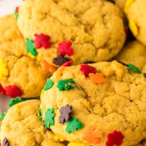 a pile of pumpkin cookies with autumn sprinkles on a round white plate.