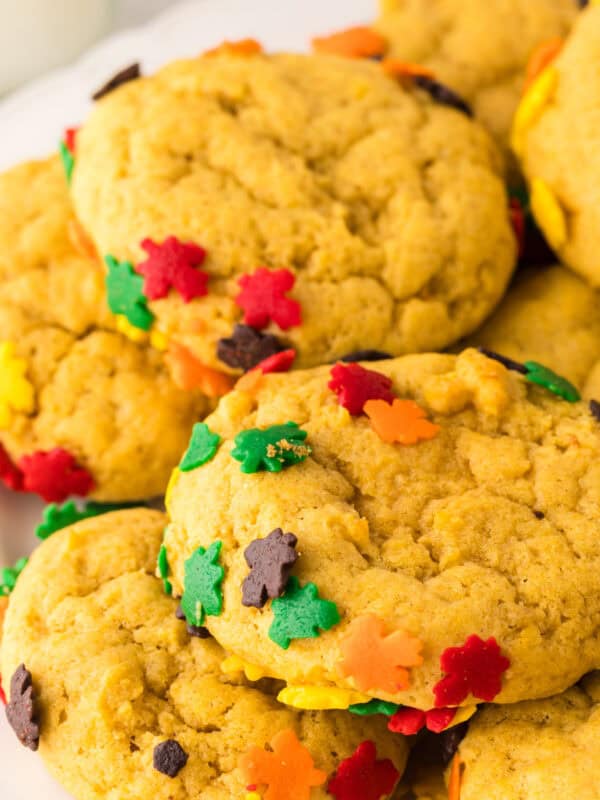 a pile of pumpkin cookies with autumn sprinkles on a round white plate.